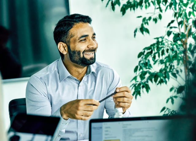 A smiling man fiddles with a pen during a meeting in a conference room.