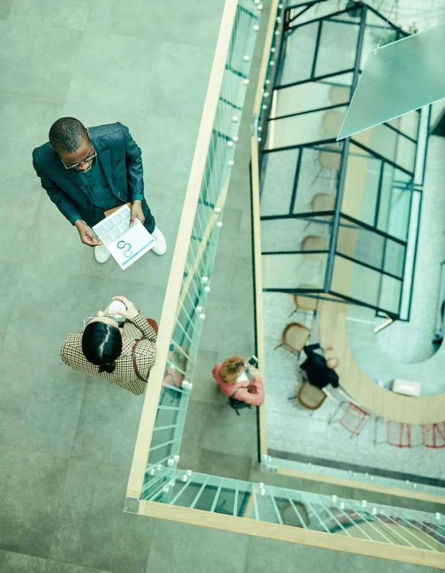 An overhead shot of two people talking on a balcony over an atrium.