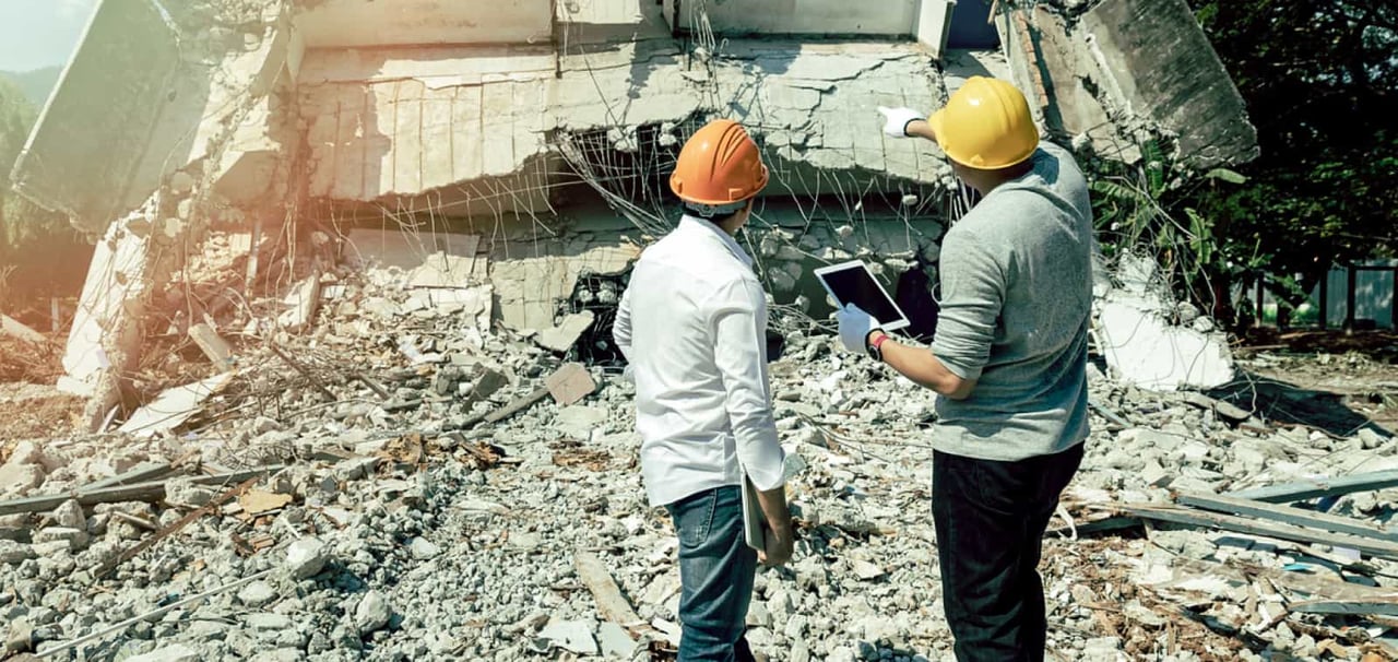 Two workers inspecting a collapsed building.