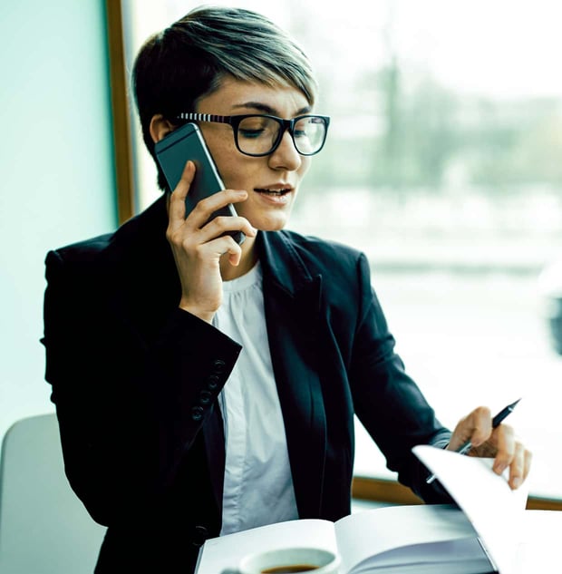 A woman in a blazer reviews papers while talking on a smartphone.