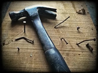 close up of hammer surrounded by bent nails sticking out of board
